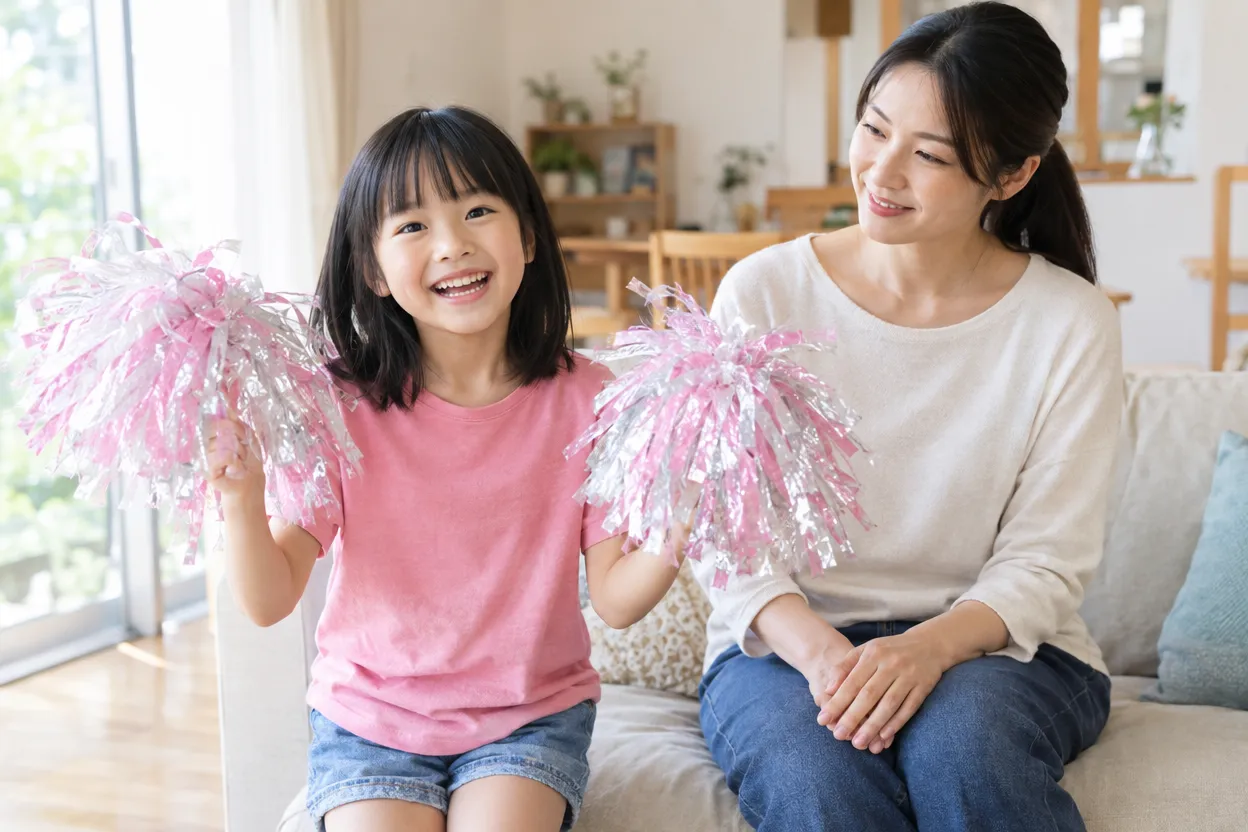 完成した手作りのポンポンを自宅で振ってみる女の子と見守る母親